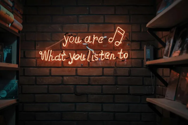 A neon sign on a wall, reading, &quot;You are what you listen to.&quot;