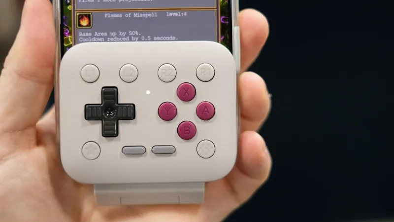 Два робота OlloBot — один с длинной пушистой фиолетовой шеей, другой стандартный — на светло-фиолетовом полу перед экраном с изображением ребёнка, играющего с кубиками