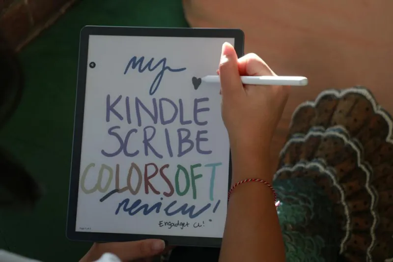 A person holding the Kindle Scribe Colorsoft in their left hand while holding the Premium Pen in their right, finishing off a drawing of a heart on the device.