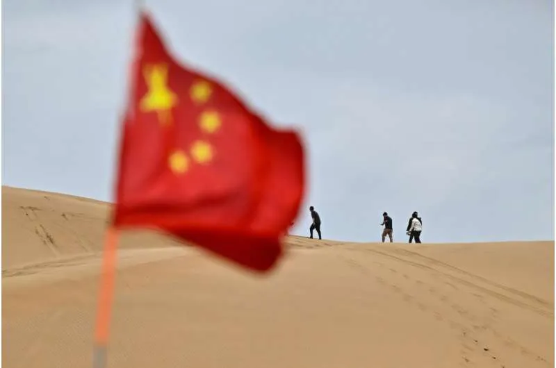 A Chinese flag flies in the desert with tourists in the background near Ordos, in China's northern Inner Mongolia region