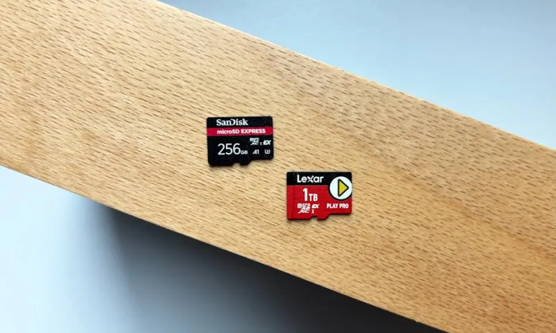 Красная карта microSD Express лежит на маленьком черном кард-ридере microSD на коричневом деревянном столе рядом с белой каменной подставкой для напитков
