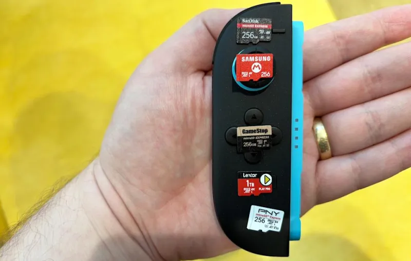 A man holds a Nintendo Switch 2 Joy-Con controller with a number of microSD Express cards placed on top of it.
